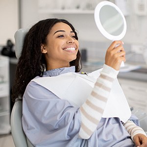 Woman smiling at reflection in handheld mirror