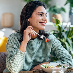 Woman in green sweater eating salad at home