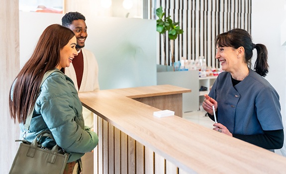 Dental receptionist smiling at couple in lobby