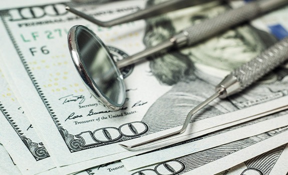 Dental tools laying on a pile of hundred-dollar bills