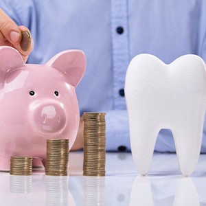 A large model tooth next to a piggy bank and various stacks of coins