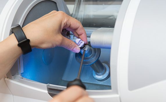 Hands removing dental crown from milling machine