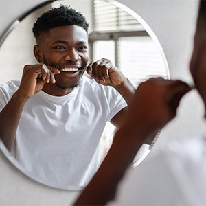 Man smiling while flossing his teeth in bathroom